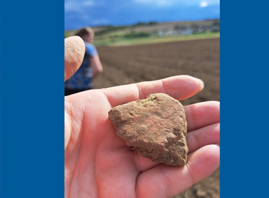 Ein Stück Bandkreamik liegt in einer Hand im Hintergrund ist ein Feld zu sehen...
