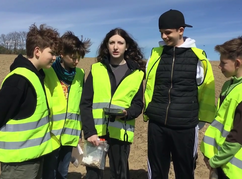 Schülerinnen und Schüler stehen auf einem Feld, haben Fundstücke und ein Tablet...