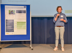 Katharina Auer Voigtländer steht auf der Bühnen neben ihrem wissenschaftlichen...