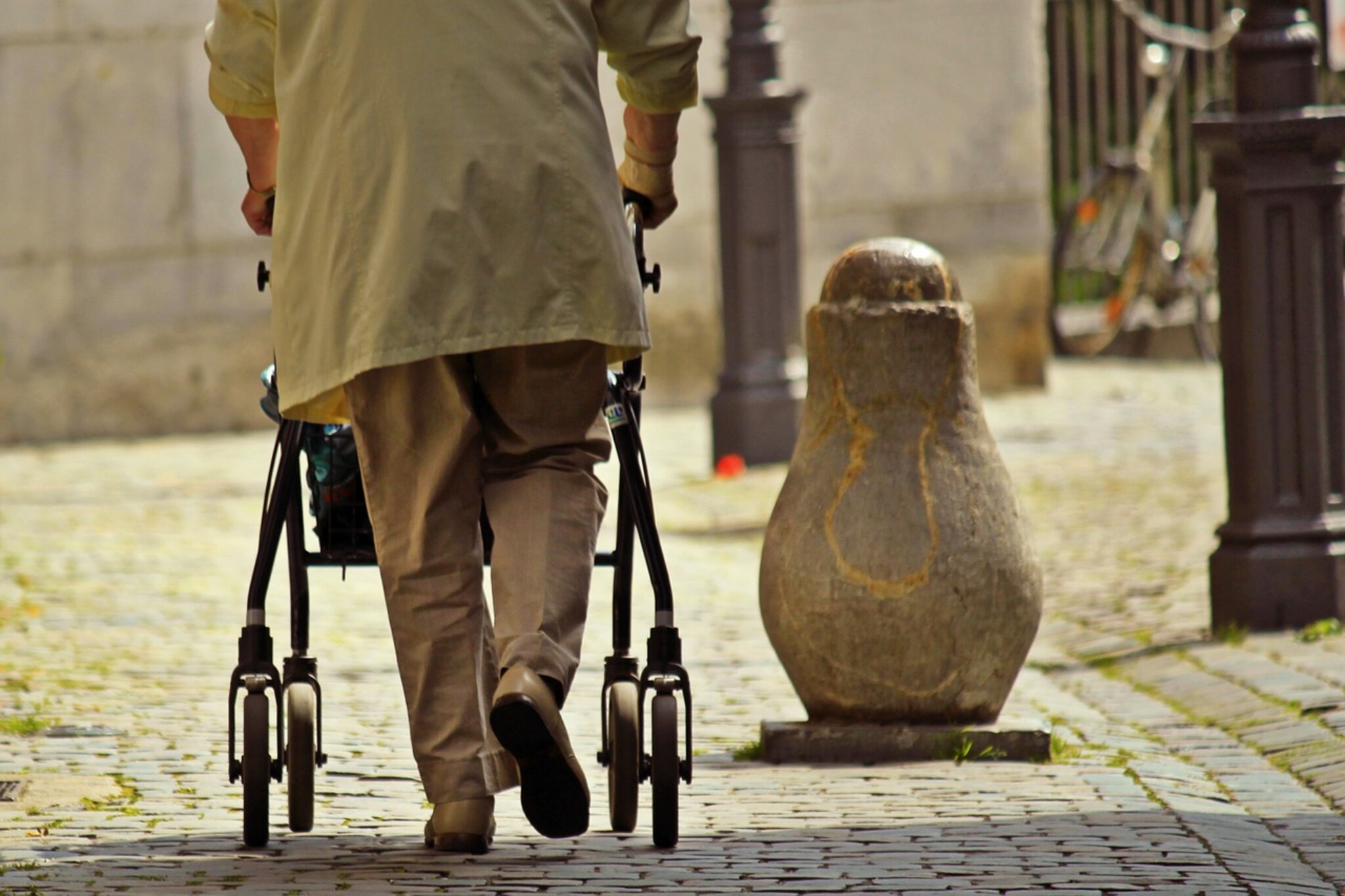 eine Person geht mit Hilfe eines Rollators über ein Kopfsteinpflaster