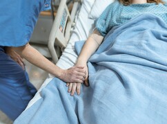 Eine Pflegerin ergreift die Hand einer zu pflegenden Frau am Krankenbett