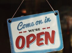 Ein Schild mit 'Come on in we are open' hängt auf einer Tür