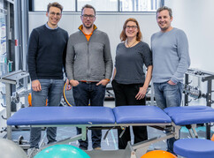 Die Forscher*innen stehen vor eine Liege in einem Physiotherapie Behandlungsraum