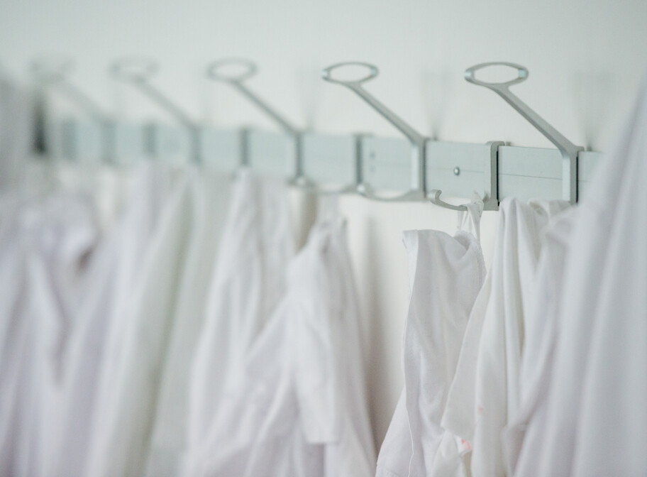 eine Reihe weißer Mäntel hängen an der Garderobe