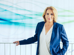 Frau Mag. Prommer steht vor einem Geländer und lächelt in die Kamera